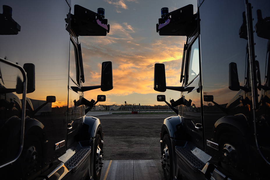 Two heavy goods vehicles sit side by side with clouds lit up by a sunset in between.