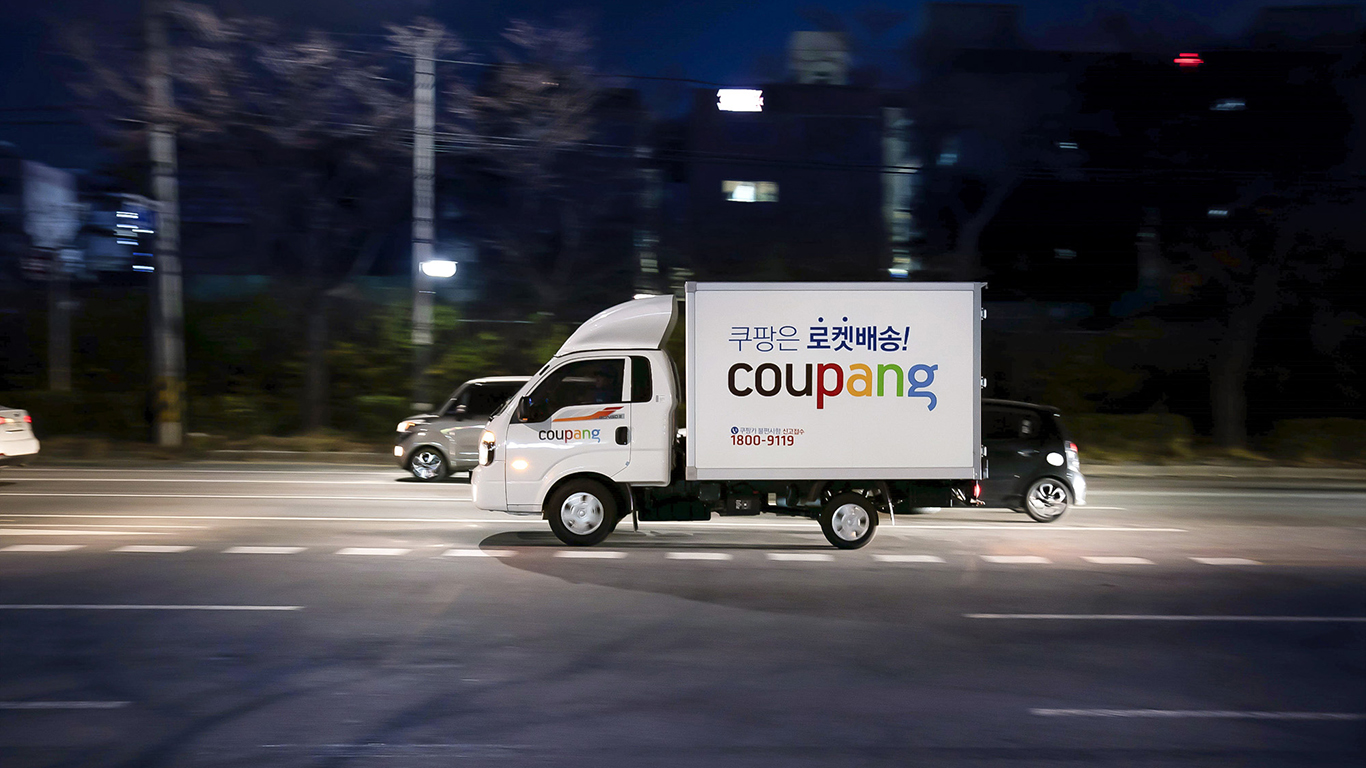 A Coupang branded truck drives on a road at night time.